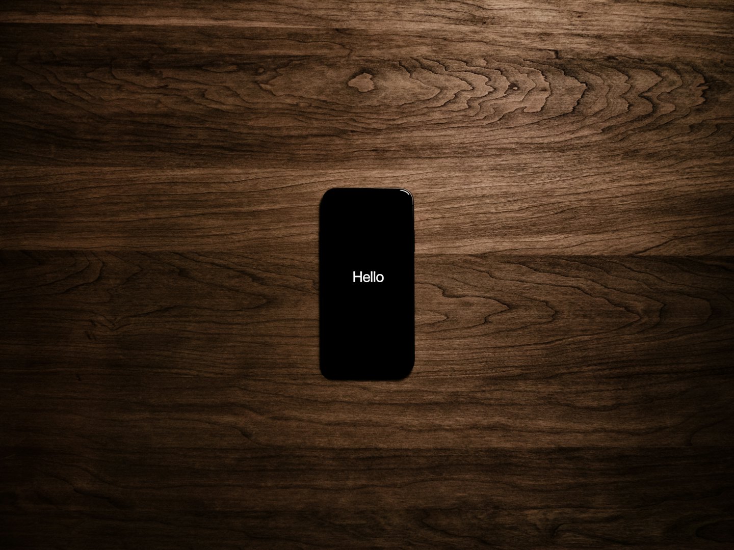 Black smartphone with Hello on the screen sits on wood.