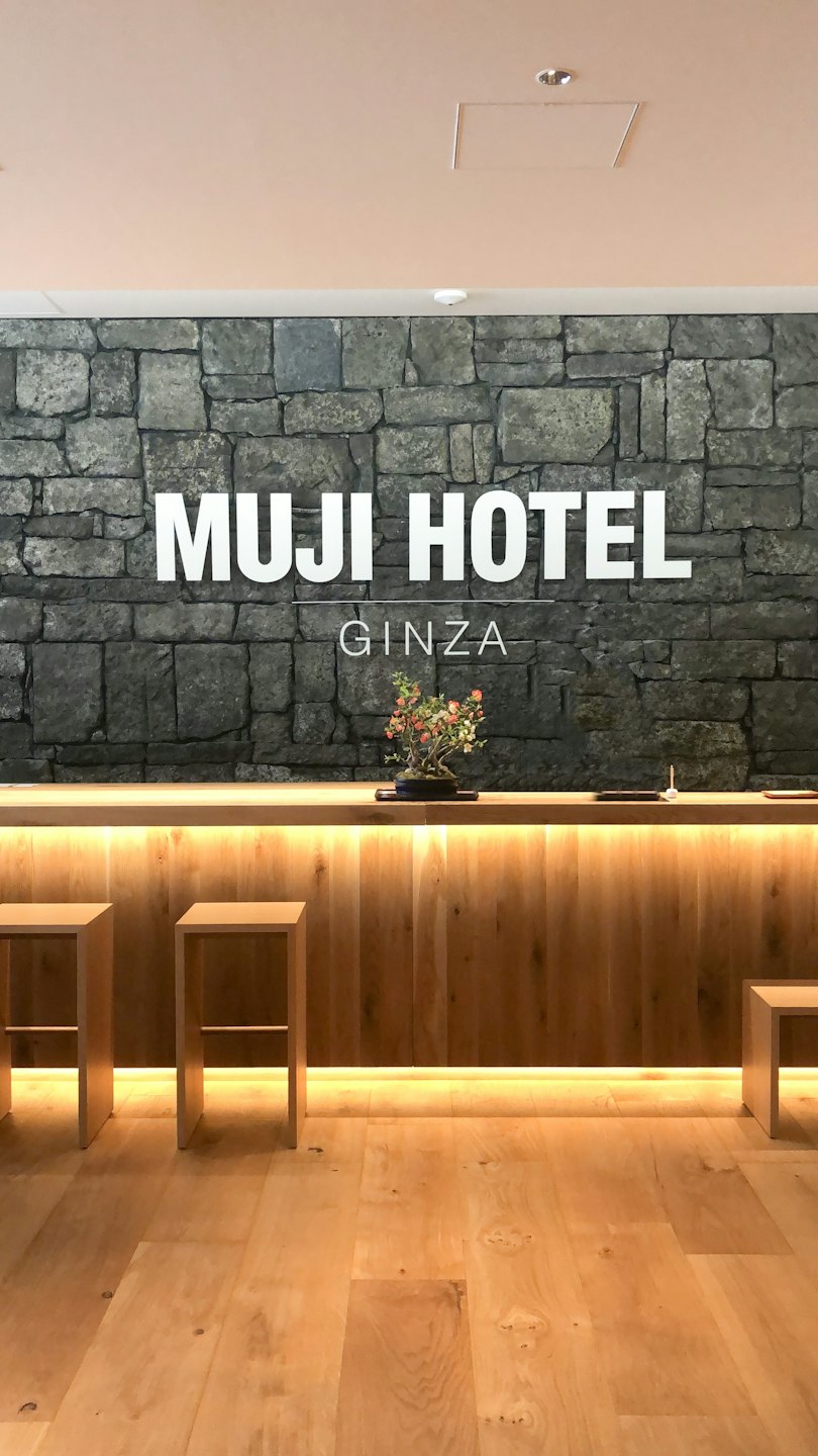 Hotel reception desk with a wooden counter and grey stone wall.