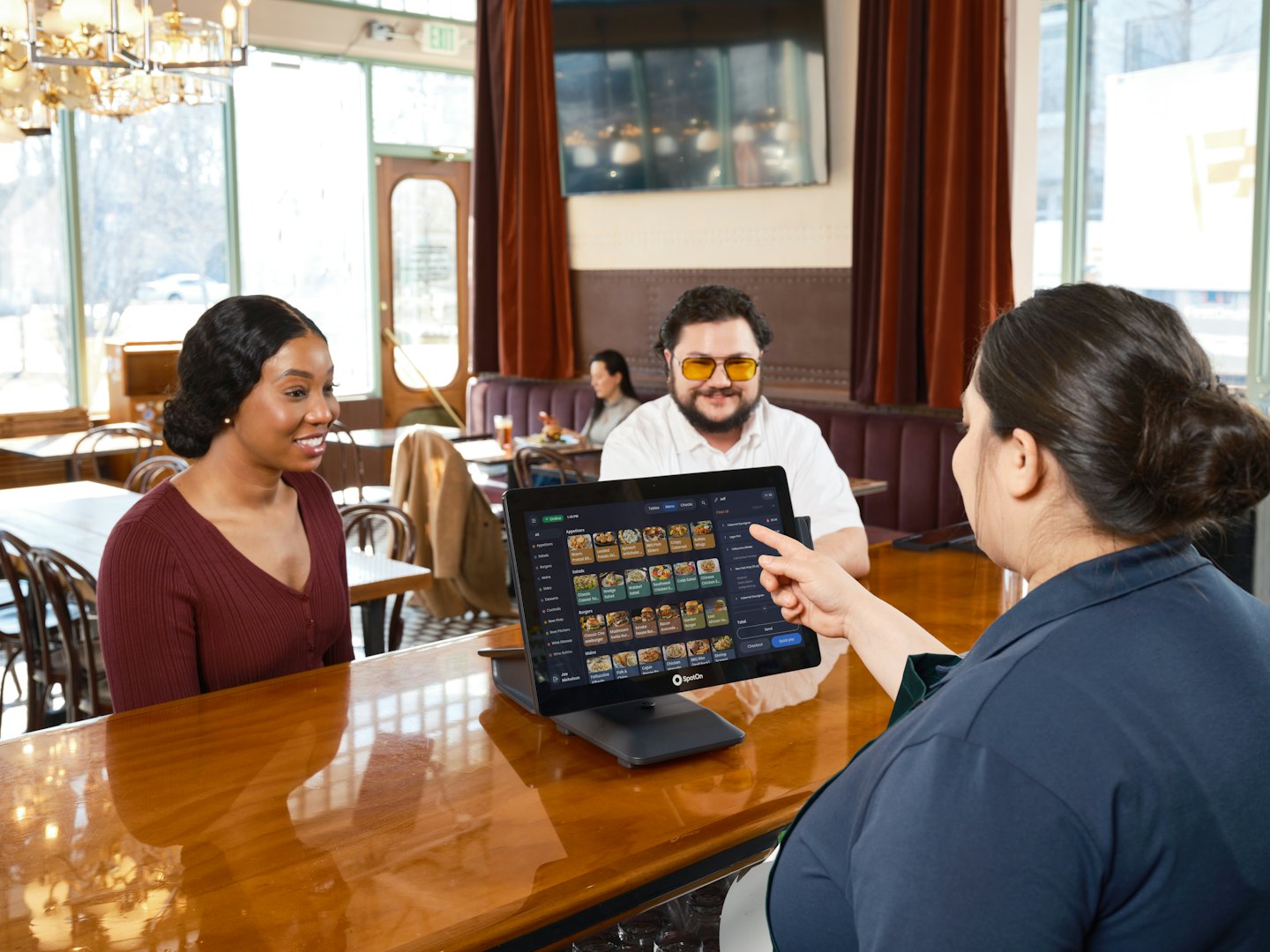 Staff member shows a digital tablet menu to two customers.